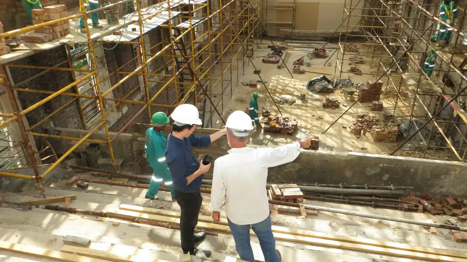 Twee mannen met bouwhelm bekijken een gebouw in renovatie met steigers